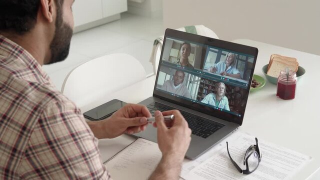 Latin indian businessman having virtual team meeting group call chatting with diverse people in customer support. Video conference call on computer with manager andemployees. Over shoulder view.