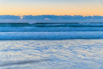 Fototapeta na wymiar Clear skies sunrise seascape with waves and a low cloud bank on the horizon