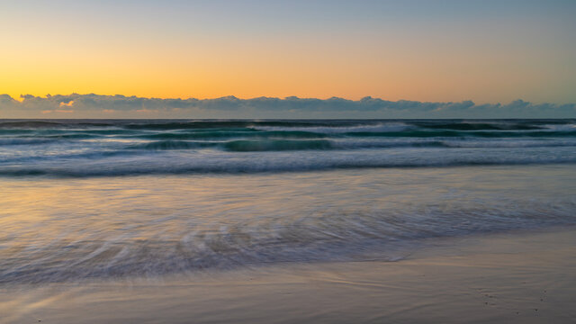 Clear skies sunrise seascape with waves and a low cloud bank on the horizon