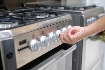 Male hand turning temperature knob of modern oven in kitchen showroom. Buying cooking appliance for...