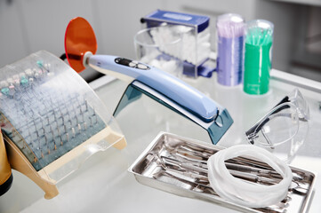 Fototapeta na wymiar Close-up snapshot of dental instruments. Glass table in dentist office with all necessary tools for teeth treatment: UV lamp, drill heads, glasses, cheek retractor, steel hooks