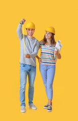 Young couple with house plans and measuring tape on color background