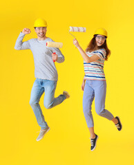 Young couple with paint rollers jumping on color background