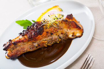 Roasted spicy pork ribs served on white plate in chocolate sauce with baked potatoes and greens