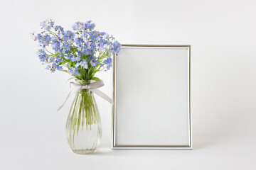 Large A4 silver frame mockup template with blue forest flowers in glass vase on the right side on white background.