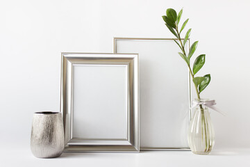 Minimalist stylish composition mockup template with two silver blank frames, zamioculcas plant in glass vase and empty silver pot.