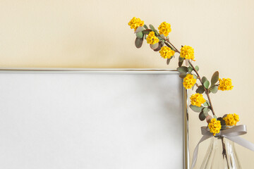 Closeup of large silver blank frame canvas with yellow plant flower in glass vase with satin bow.