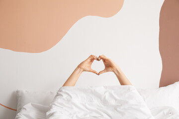 Young woman making heart with her hands in bedroom