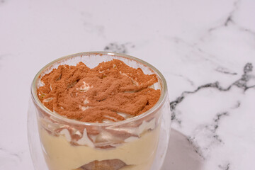Tiramisu In A Glass Container Against A White Marble Countertop