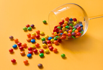 Colorful candies in a glass on yellow background