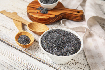 Bowl and spoon with poppy seeds on light wooden background