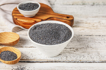 Bowl and spoon with poppy seeds on light wooden background