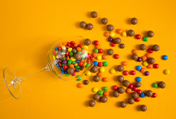 Colorful candies in a glass on yellow background