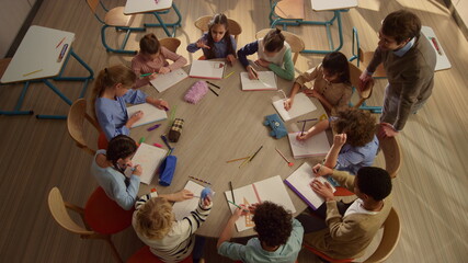 Schoolchildren having lesson at round table. Male teacher helping kids at lesson