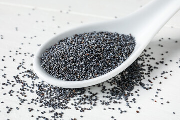 Spoon with poppy seeds on light wooden background