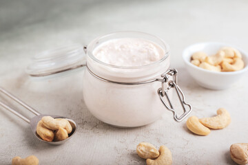 Jar with cashew sour cream and nuts on light background, closeup