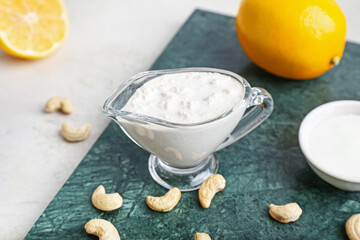 Gravy boat with cashew sour cream, nuts and lemon on light background