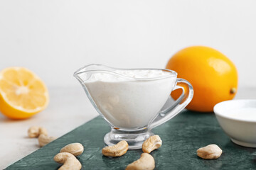 Gravy boat with cashew sour cream, nuts and lemon on light background, closeup