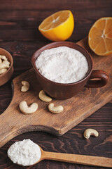 Cup with cashew sour cream, nuts and lemon on wooden background