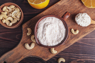 Cup with cashew sour cream, nuts and lemon on wooden background