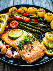 Roasted salmon steak with roast potatoes and vegetable salad served on black plate on wooden table
