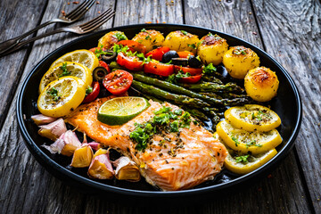 Roasted salmon steak with roast potatoes and vegetable salad served on black plate on wooden table
