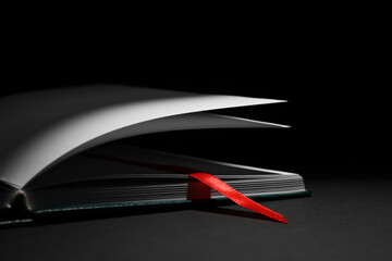 Open book with bookmark on dark background, closeup