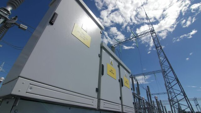 Capacitor banks in metal cabinets with yellow warning signs by towers at electricity distribution substation extreme closeup