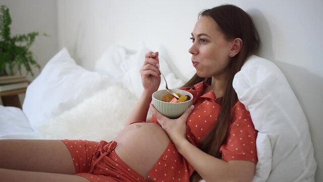 Pregnant woman eat fruit cut in salad in bed, morning breakfast of expecting future mother Spbd