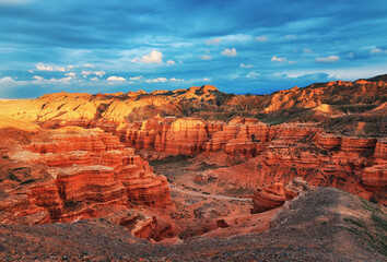 The view from the top to the canyon, sunset sky, erosion, plateau, cloudy sky and mountains on the horizon. Red rocks and layers. Panorama of the Charyn canyon in Kazakhstan.