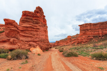 Canyon, mountain erosion, plateau, cloudy sky and mountains on the horizon. Red rocks and layers. The road along the bottom of the canyon. Charyn canyon in Kazakhstan