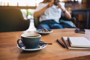 Closeup image of coffee cup and books on wooden table with woman sitting in background