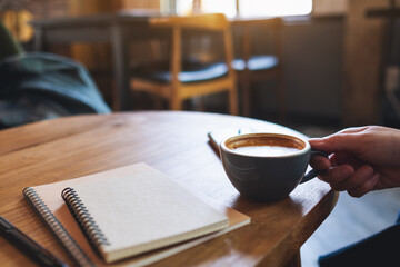 Closeup image of a woman holding coffee cup with notebooks on wooden table