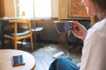 Closeup image of a beautiful young asian woman holding and drinking hot coffee