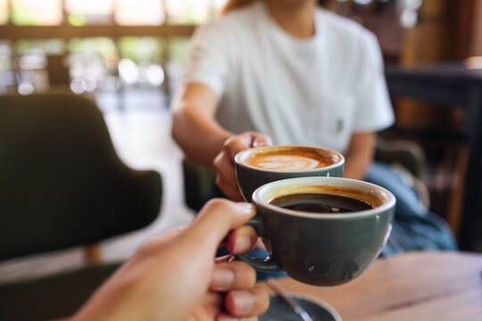 Closeup image of a man and a woman clinking coffee mugs in cafe