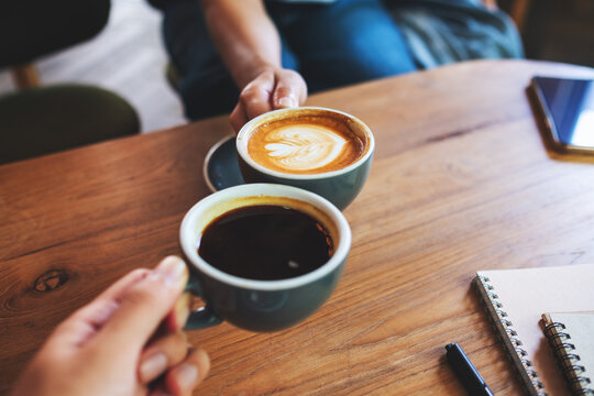 Closeup image of a man and a woman clinking coffee mugs in cafe