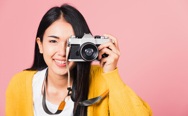.Attractive energetic happy Asian portrait beautiful young woman smiling photographer taking a picture and looking viewfinder on retro vintage photo camera ready to shoot isolated on pink background
