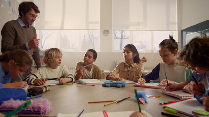 Teacher explaining lesson to schoolchildren. Students writing in exercise books 