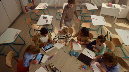 Pupils with pads studying at round table. Children using digital tablets