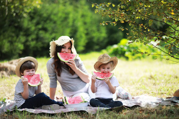 Happy family with children having picnic in park, parents with kids sitting on garden grass and eating watermelon outdoors