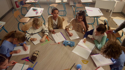 Children studying at round table in class. Teacher talking with students 