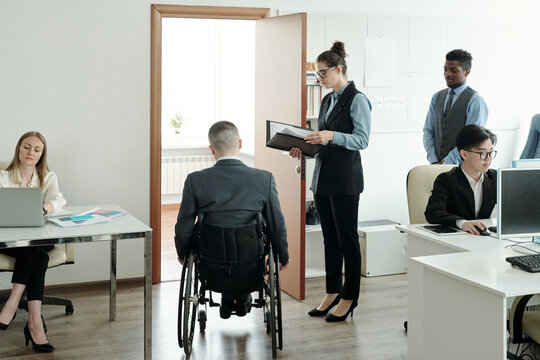 Secretary With Papers Waiting For Boss In Wheelchair Entering His Office