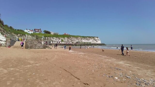 People chilling at Dumpton Gap bay with colourful wooden beach huts between Broadstairs and Ramsgate