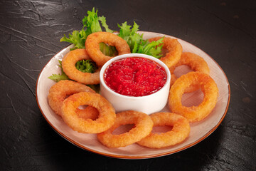 Calamari rings. Deep fried squid rings with lettuce leaves and ketchup on a black background