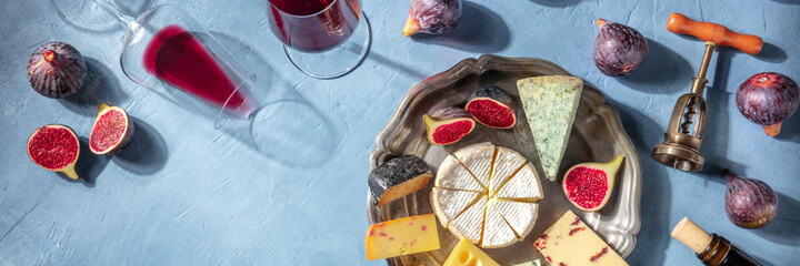 Red wine and cheese board panoramic header with a place for text, shot from above on a blue background. Romantic French menu