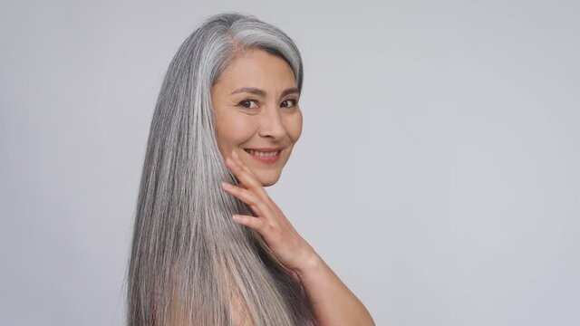 Middle aged gorgeous happy mature asian woman, senior 50 year lady, smiling looking at camera, touching silver hair isolated on white. Ads of antiaging whitening dry skincare, plastic surgery.