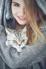 Woman at home with her lovely fluffy cat. Gray cute kitten with green eyes. Animals and lifestyle concepts. High quality photo.