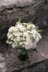 Beautiful bridal bouquet of white flowers and greenery, decorated with long silk ribbon lies on a gray textural background. Copy space