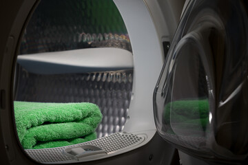 Dryer with open door in a dark room. Green towels are stacked inside the drum.