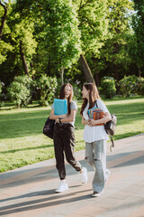 Two happy smiling student girls are walking and talking to each other on campus on a warm sunny day. Soft selective focus.